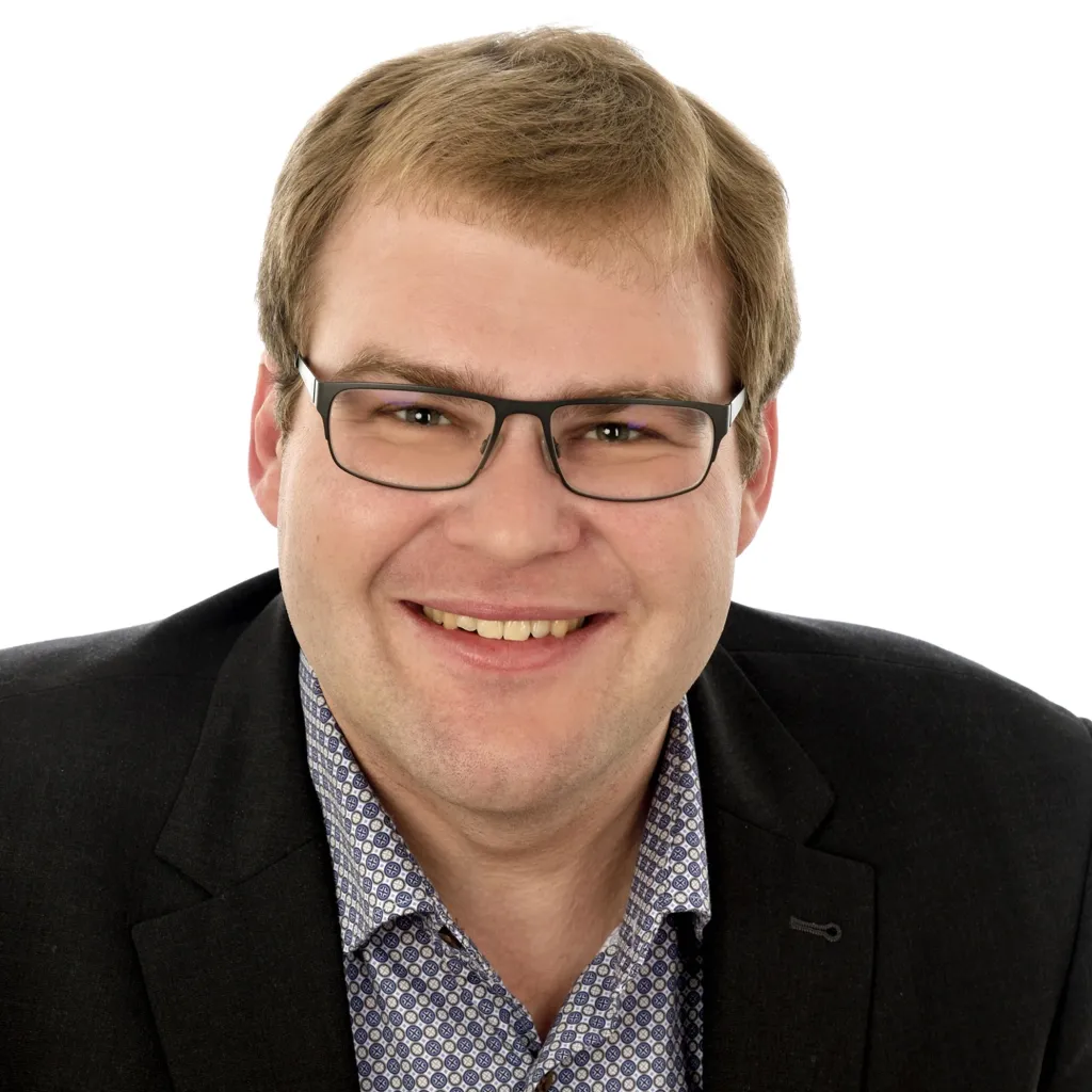 Portraetfoto von Christoph Müller mit schwarzem Sacko und kariertem Hemd